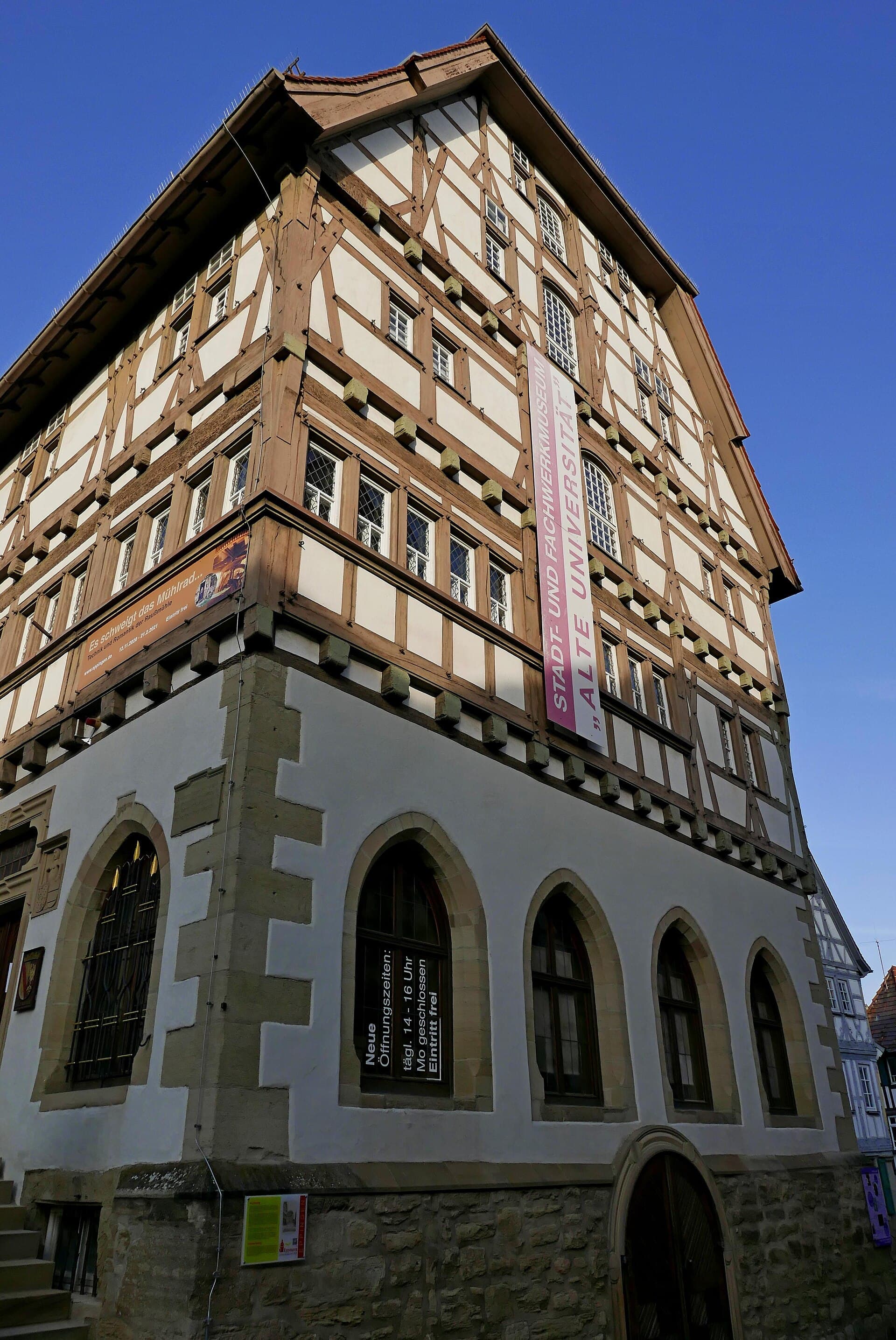 Die Alte Universität in Eppingen von der Straßenecke aus gesehen: steinernes Erdgeschoss mit Spitzbogenfenstern, darüber vier Stockwerke Fachwerk unter einem steilen Dach.