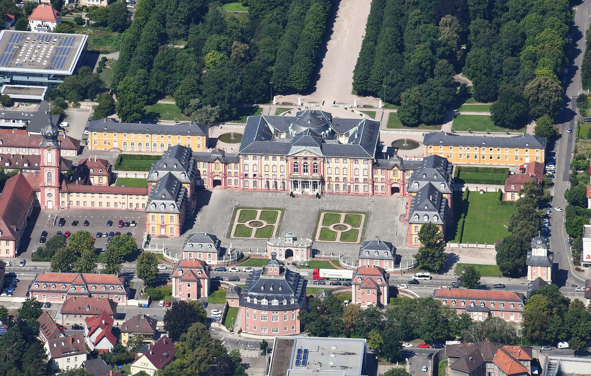 Luftbild von Osten auf Schloss Bruchsal mit Ehrenhof, Mittelbau und Seitenflügeln, links der Turm der Hofkirche, dahinter die baumgesäumte Mittelachse des Schlossgartens und vorn die Schönbornstraße.