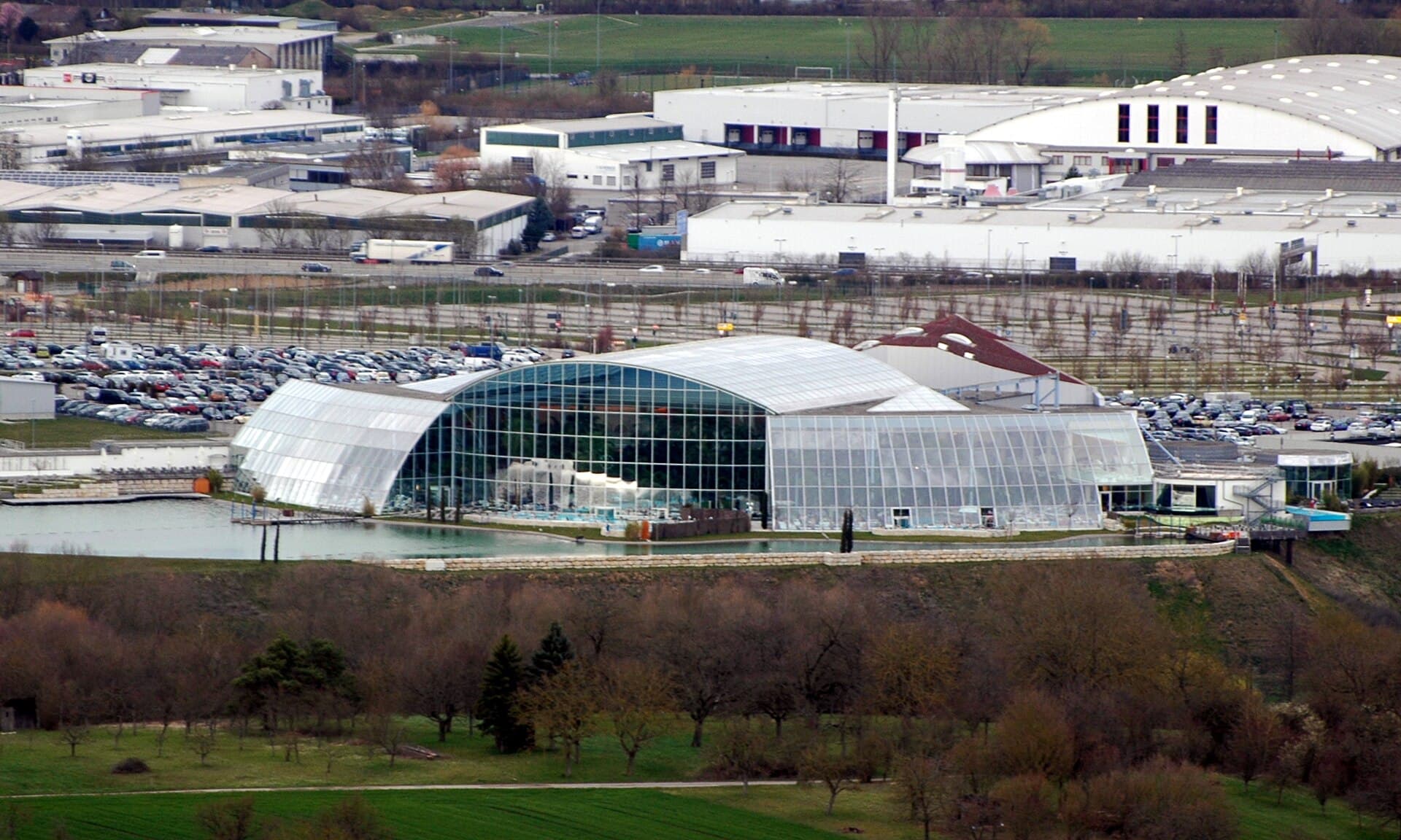 Die Glashallen der Thermen & Badewelt Sinsheim am Natursee, von der Burg Steinsberg aus gesehen, dahinter Parkplätze und das Gewerbegebiet Sinsheim-Süd