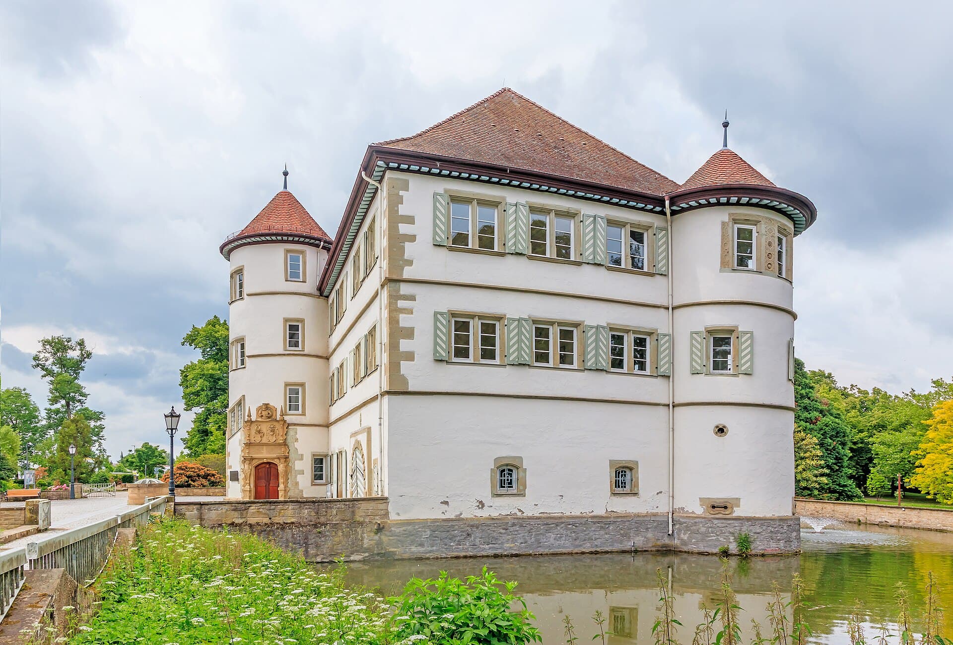 Das weiß verputzte Wasserschloss Bad Rappenau mit zwei runden Türmen, links das verzierte Portal am Treppenturm, davor der Wassergraben mit einer Fontäne.