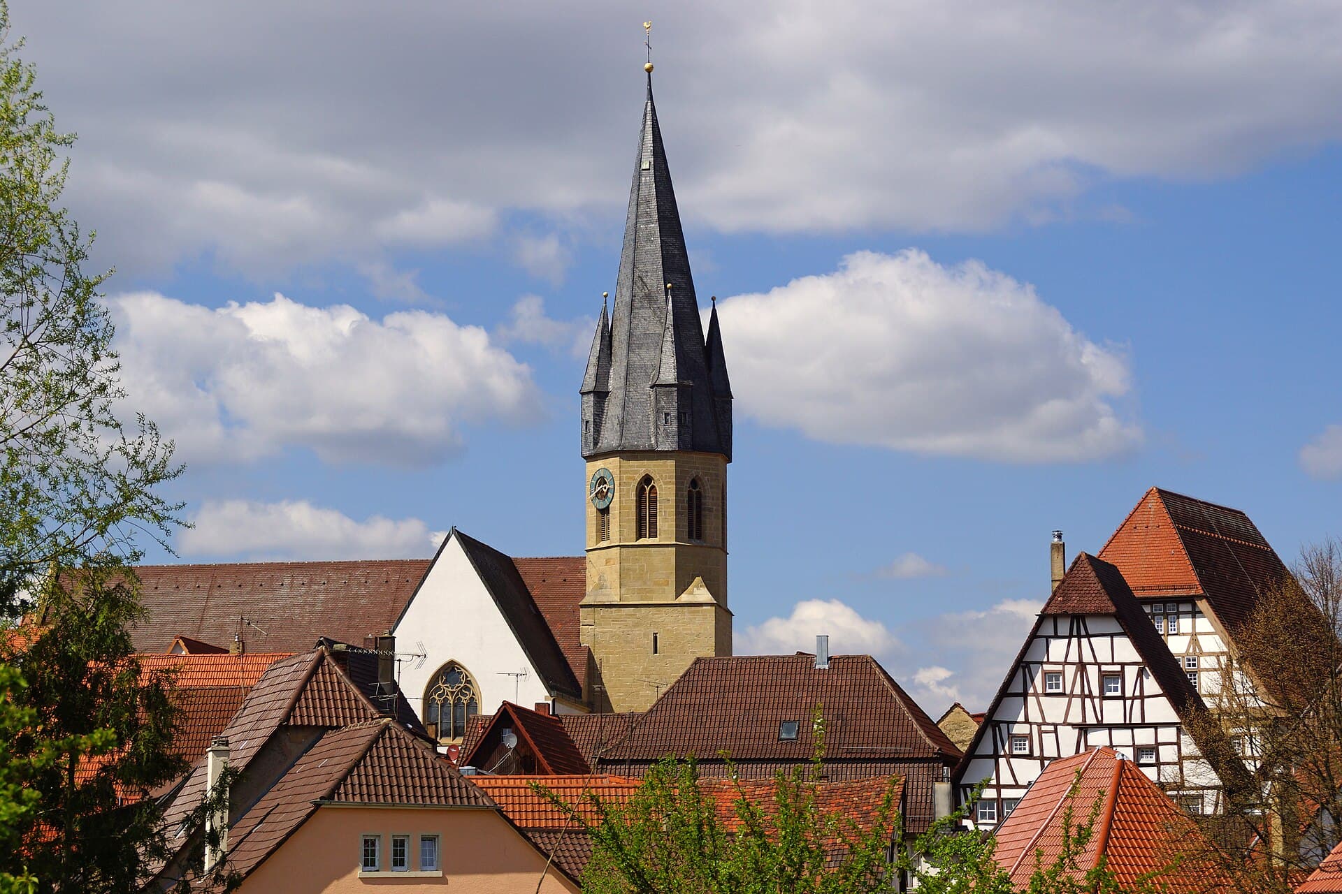 Blick über rote Ziegeldächer der Eppinger Altstadt auf den spitzen, schiefergedeckten Turm der Stadtkirche Unsere Liebe Frau, rechts zwei Fachwerkgiebel