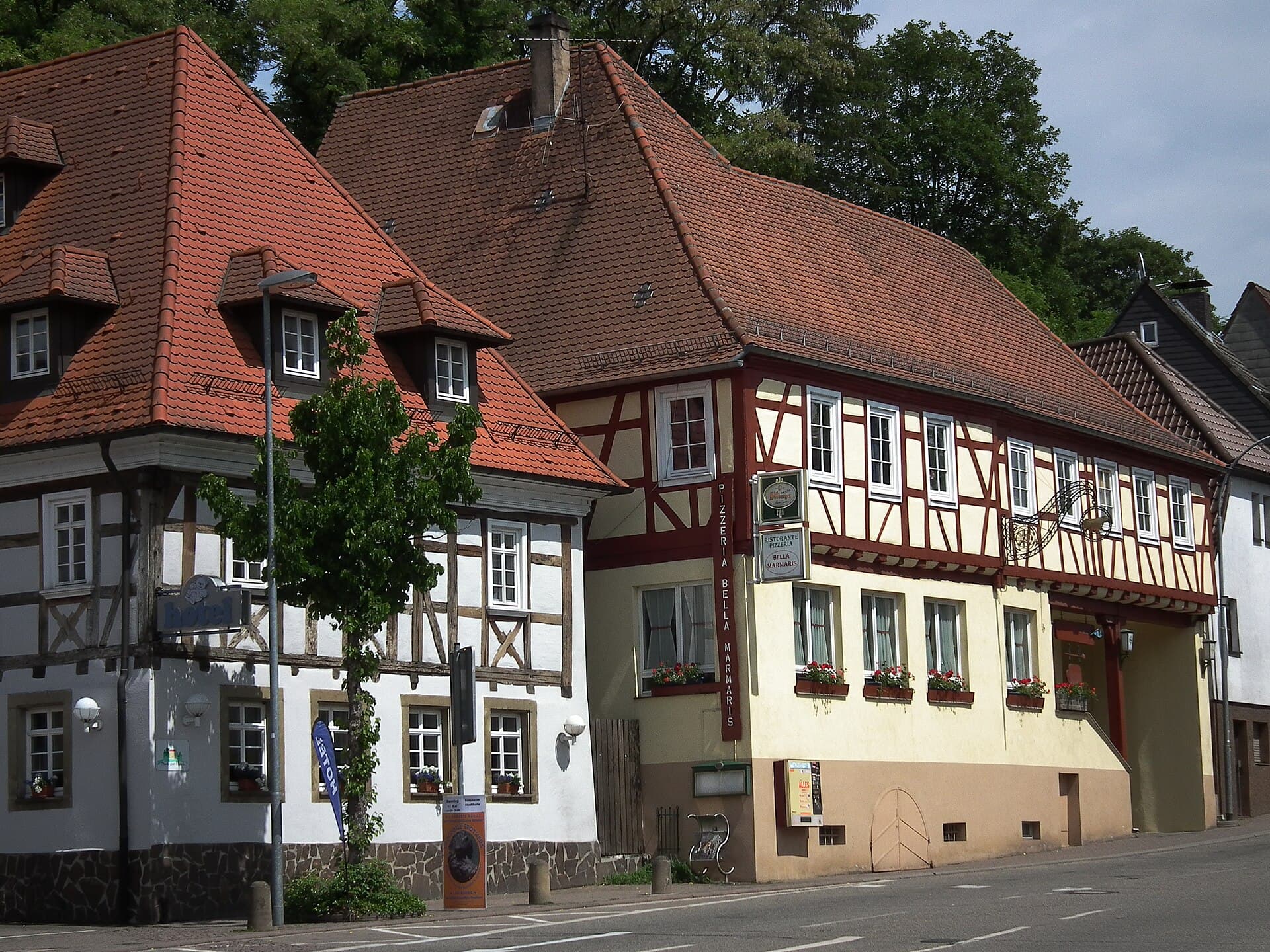 Zwei Fachwerkhäuser mit roten Ziegeldächern an der Hauptstraße in der Sinsheimer Innenstadt, links ein weiß verputztes Haus mit Gauben, rechts ein gelb und rot gestrichenes Fachwerkhaus mit Blumenkästen.