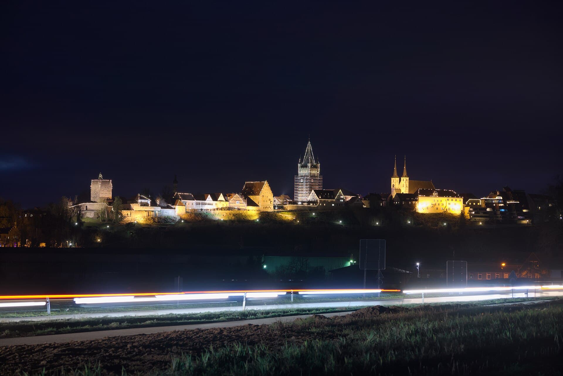 Die Altstadt von Bad Wimpfen am Berg an einem Dezemberabend mit Weihnachtsbeleuchtung, angestrahlt Roter Turm, Steinhaus, der eingerüstete Blaue Turm und die Türme der Stadtkirche, im Vordergrund Lichtspuren auf der B 27