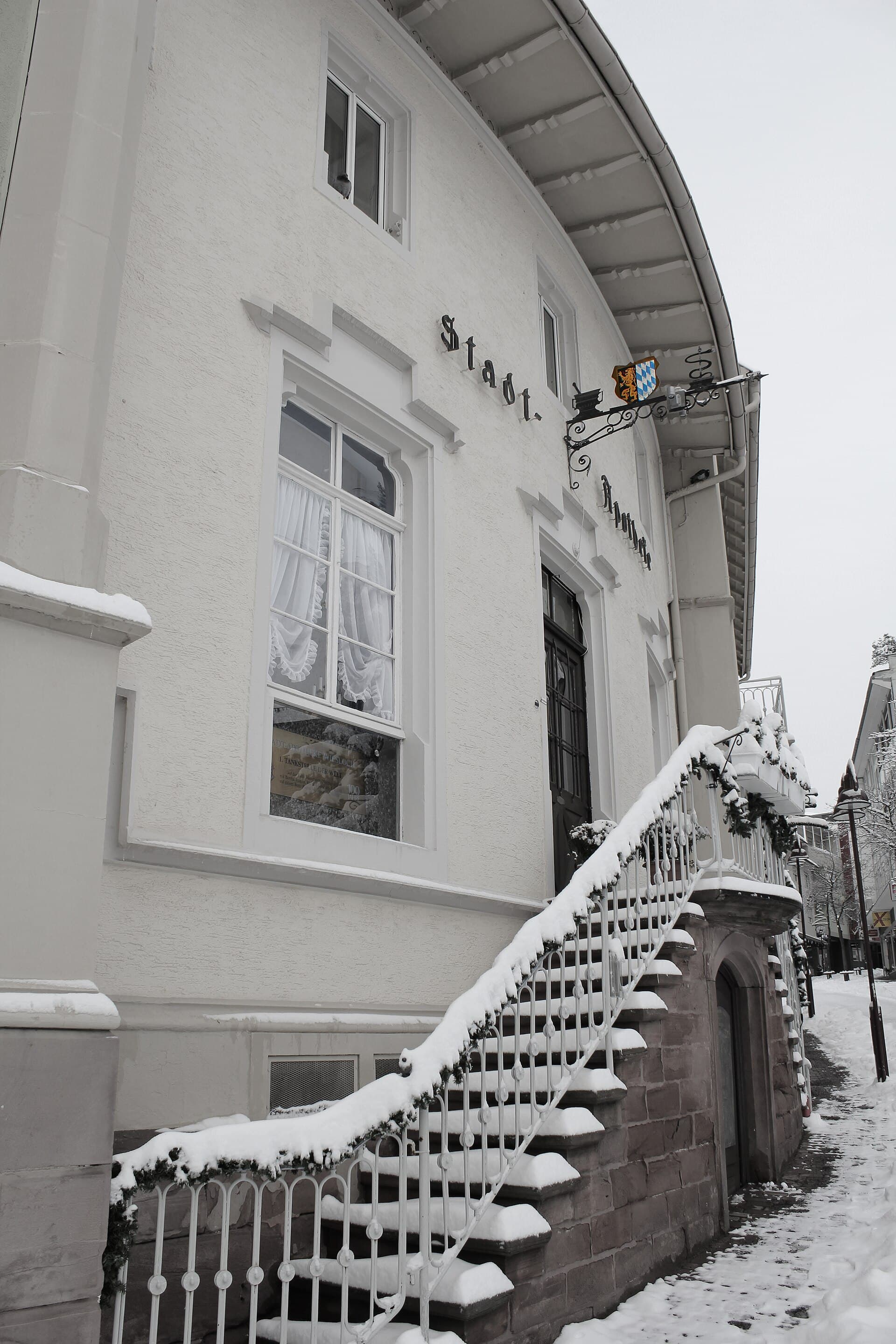 Die Stadt-Apotheke in der Wieslocher Hauptstraße an einem verschneiten Wintertag: weiße Fassade mit Schriftzug und schmiedeeisernem Schild, davor eine Freitreppe mit Tannengirlande am Geländer.