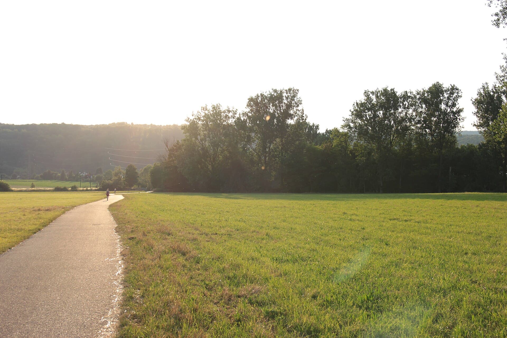 Ein schmaler asphaltierter Radweg führt im Abendlicht durch Wiesen und Auwald im Elsenztal bei Mauer, in der Ferne zwei kleine Gestalten